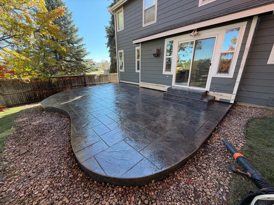 Ashlar Cut Slate stamped concrete patio with charcoal-gray coloring, curved borders, and decorative rock landscaping at a Ken Caryl home.