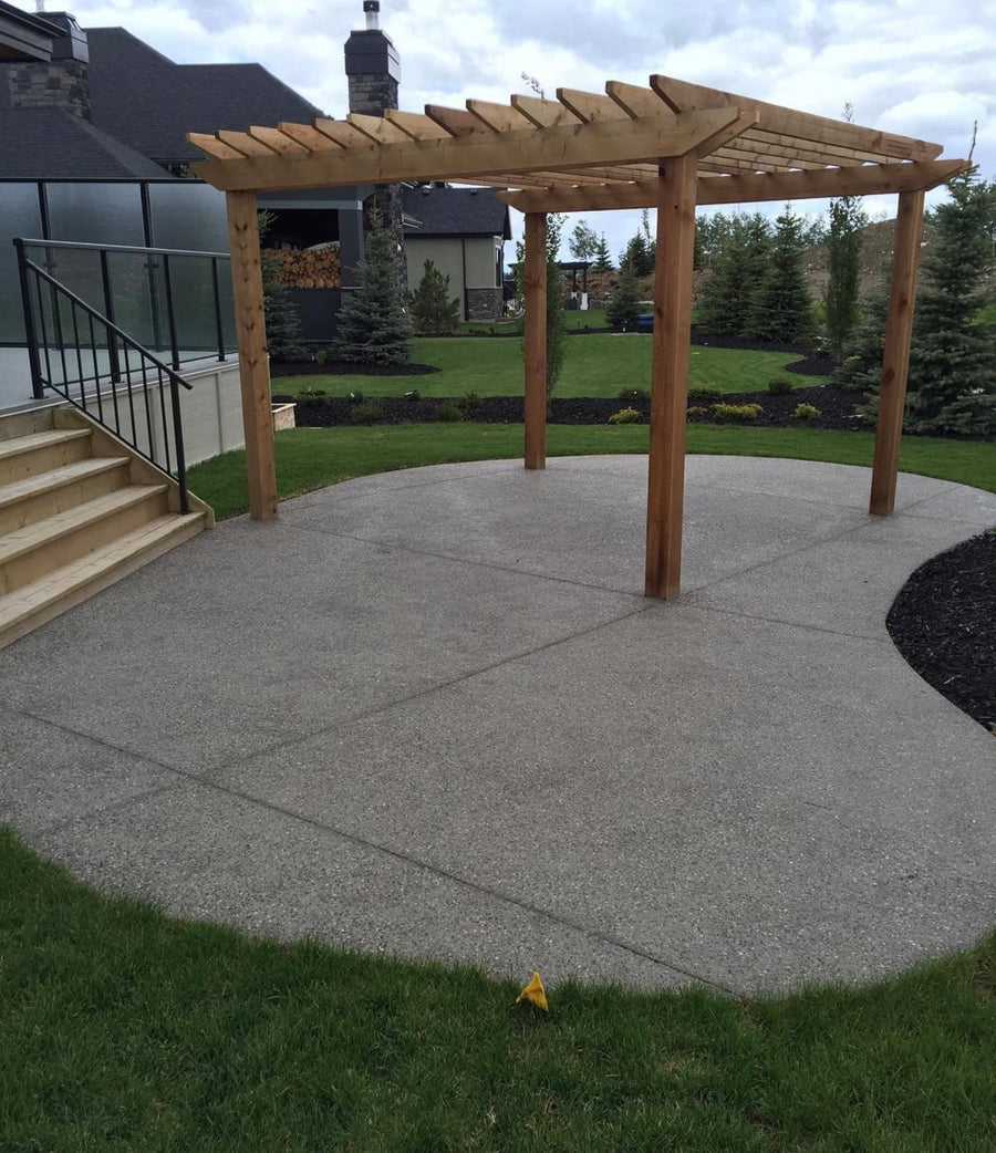 Curved exposed aggregate concrete patio with wooden pergola and landscaped backyard